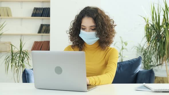 Young Business Woman in a Medical Protective Mask Works From Home at the Computer During