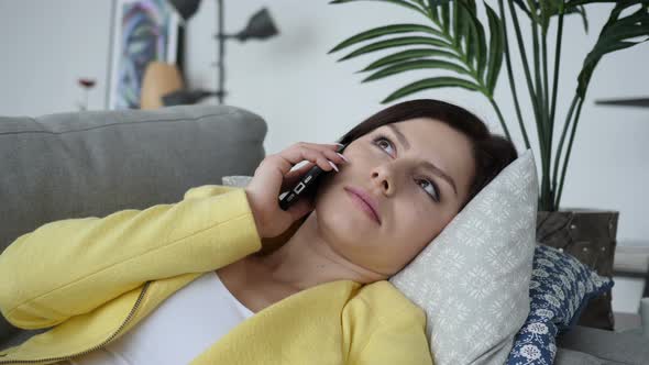 Young Woman Talking on Phone while Laying on Sofa at Home