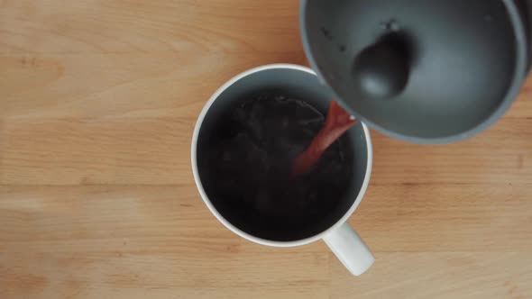 Pouring black coffee from a French Press to a white cup on a wooden cutboard