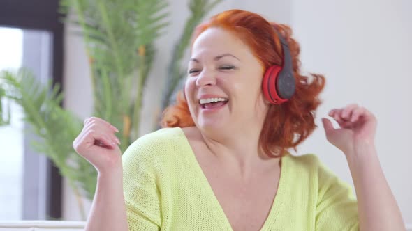 Joyful Relaxed Redhead Woman Enjoying Music in Headphones Indoors