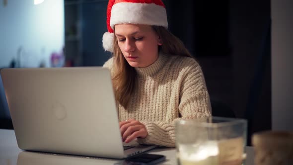 A Young Woman Wearing a Santa Hat Works Hard on a Laptop From Home