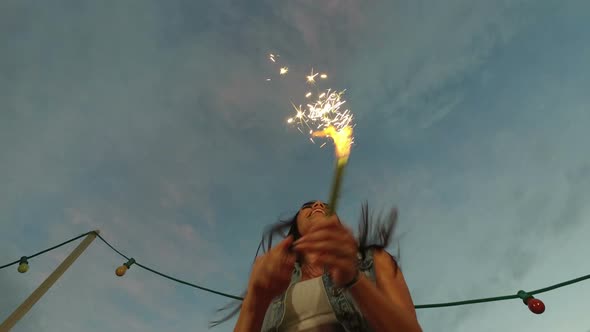 Low angle view of happy woman jumping with firework candle