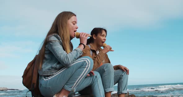 Side view of a Caucasian and a mixed race girl eating ice cream seaside