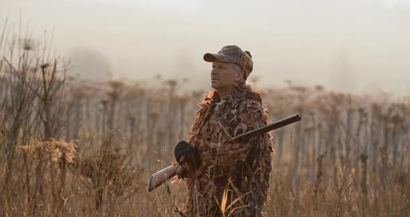 Portrait of Hunter with Shot Gun Standing in the Field and Looking Around, Foggy Autumn Morning