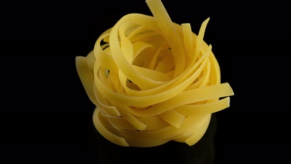 Raw Italian Pasta tagliatelle on black background, rotation