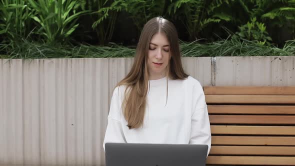 Young Female in Garden Using Laptop Communicates on Internet with Customer