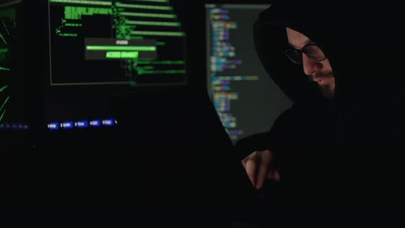 Hooded Hacker Typing Various Codes on Modern Laptop