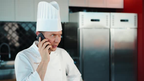 The chef is talking on the phone in the kitchen.