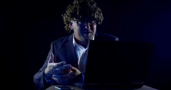 Adult Man with Funny Hair Curls and Glasses at Night Is a Video Broadcast on the Internet Via a