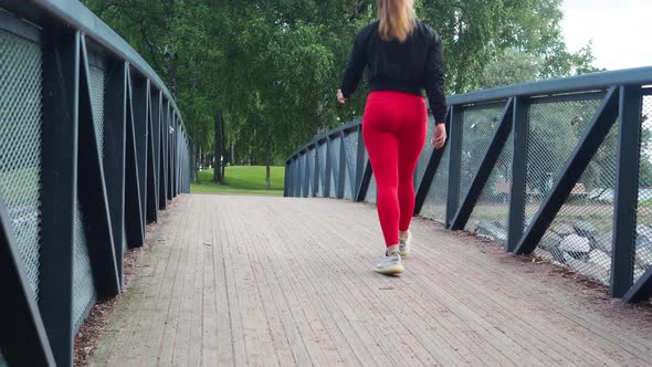 Young girl walking across a bridge in a park. Shot from behind in the back.