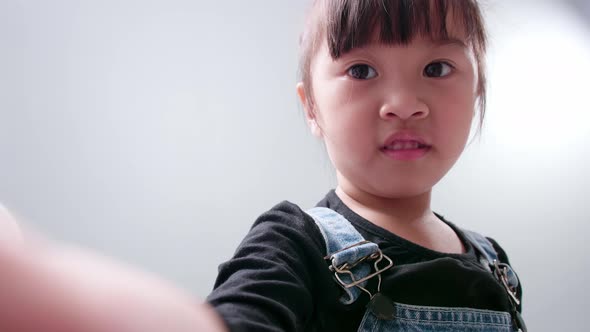 Happy little Asian girl using a smartphone for video call, waving hand and speaking and talking with