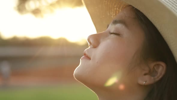 Beautiful Asian woman enjoying peaceful sunset and looking up exhaling fresh air relaxing outdoors.