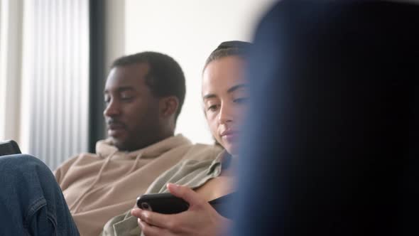 Young Couple At Home Sitting On Sofa Checking Social Media On Mobile Phones But Ignoring Each Other