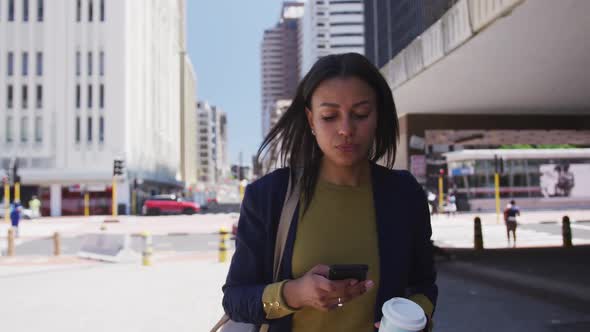 African american woman holding coffee and using smartphone in street