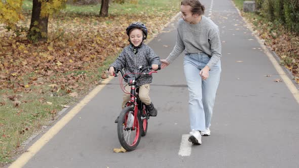 Happy Mother teaches child son to ride a bike on the bike path.