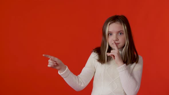 A Beautiful Caucasian Girl on a Red Background Makes a Gesture of Silence Puts Her Index Finger to