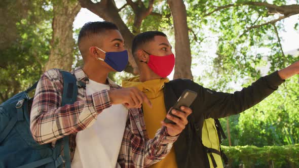 Two happy mixed race male friends using smartphone in park with backpacks