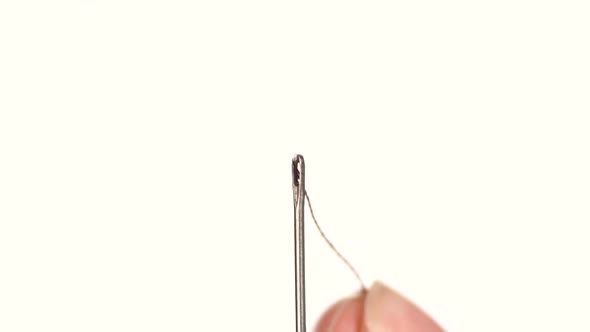 Light Thread Going Through a Needle Hole on White Background, Close Up, Slow Motion