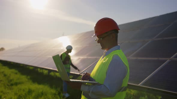 Portrait of a Male Solar Engineer Standing Uses a Tablet and Looking at the Camera Another Man