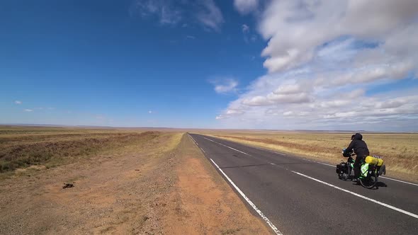 A cyclist rides on an asphalt road in the steppes of Mongolia.