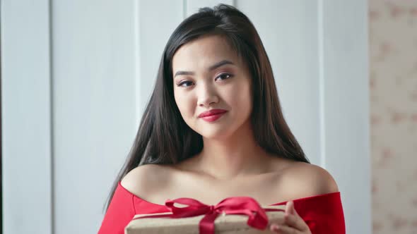 Portrait of Smiling Asian Young Woman Holding Gift Box with Red Ribbon