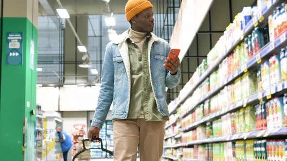 African American Guy Walks Along Grocery Shop and Types