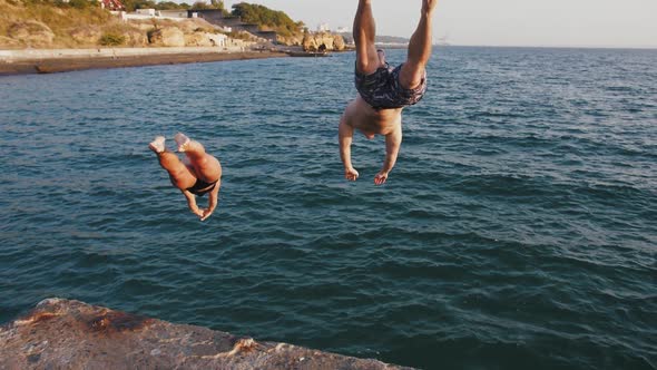 Young Woman and Man Jumping From a Pier Into the Sea During Beautiful Sunrise Super Slow Motion