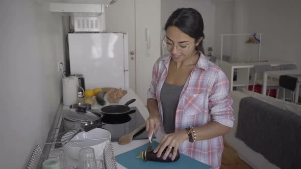 Smiling Brunette Housewife Cutting Eggplant at Kitchen Table