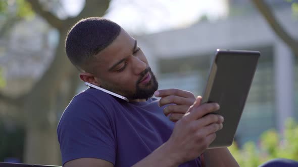 Man in Park Talking on Phone, Searching Information on Tablet