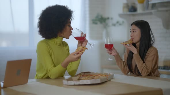 Happy Young Multinational Friends Eating Pizza and Drinking Wine in Slow Motion Indoors