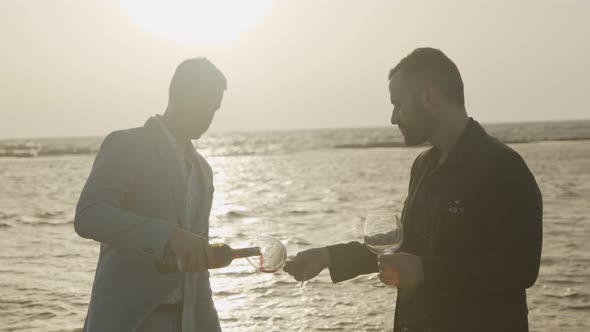 Gay couple drinking red wine on the beach during sunset