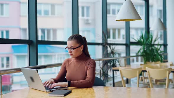 Beautiful woman assistant wearing light brown blouse working on her laptop