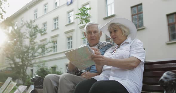 Senior Tourists Sitting on Bench with a Map in Hands Looking for Route