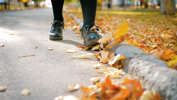 Feet of a Young Girl in Leather Shoes on Fallen Leaves in the Park. Autumn Concept.