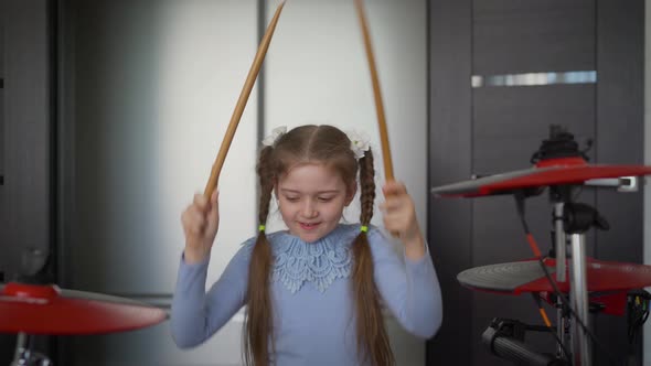 A Little Girl Plays Electronic Drums at Home. Cheerful Girl with Drum Sticks. Little Girl Playing On