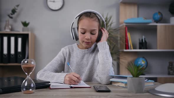 Teen Girl in Headphones which Sitting at the Table and Making Notes Into Her Diary