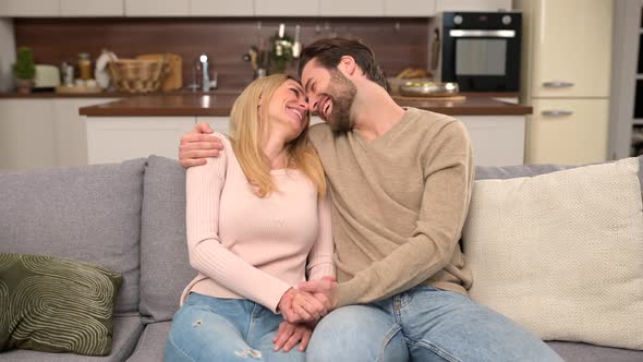 Happy Beautiful Young Wife and Husband Sitting on the Couch in Embraces