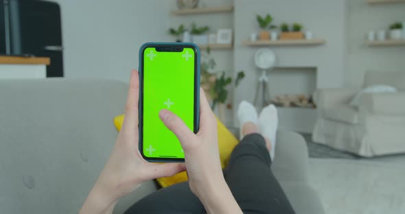 Woman at Home Lying on a Couch Using Smartphone with Green Mock-up Screen, Doing Swiping, Scrolling