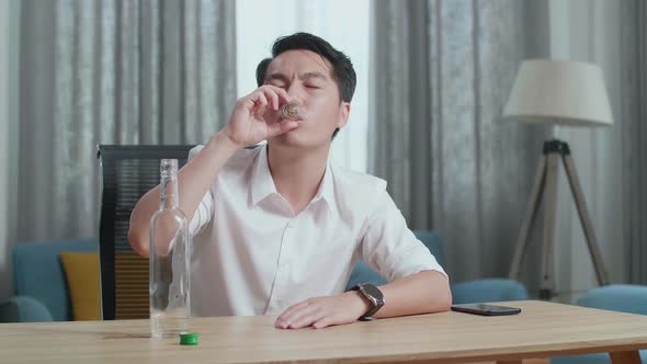 Drunk Asian Man With Smartphone On Table Pours Vodka In A Shot Glass And Cheers Before Drinking