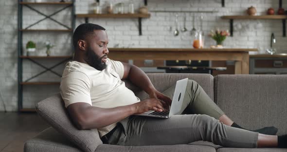 African American Businessman Distance Works at Laptop Online Chatting with Company Employees on Sofa