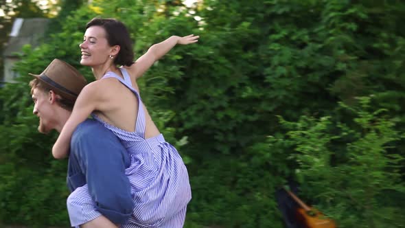 Happy Young Lovely Couple Having Fun Near Trailer in the Park Man Piggybacking Girl Running Happily