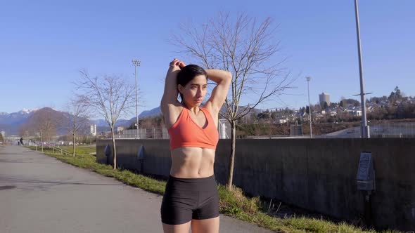 Young athletic woman stretching triceps and shoulders before outdoor workout