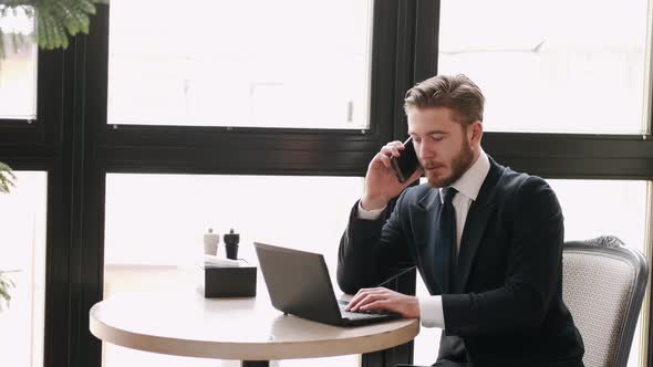 Focused Businessman Working at a Cafe with Laptop and Papers