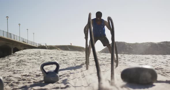 Focused african american man exercising with battling ropes outdoors on beach