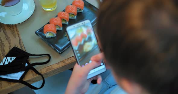 Schoolboy Makes Photo of Sushi in Restaurant Top View