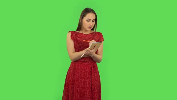 Tender Girl in Red Dress Is Standing and Thinking, Then Happy Writing with Pencil in Notebook. Green
