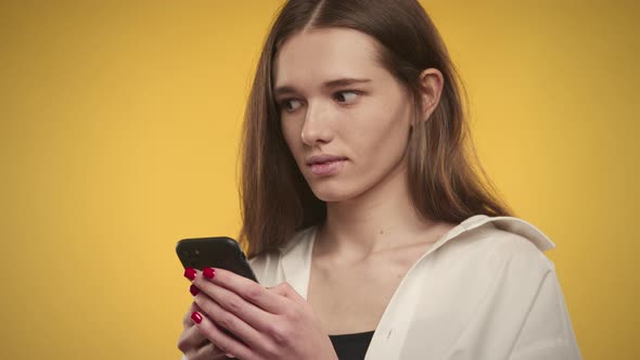 Young Adult Caucasian Woman is Thinking an Answer on Her Smart Phone on a Bright Yellow Background