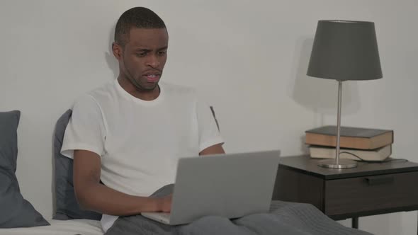 African Man Coughing While Working on Laptop in Bed