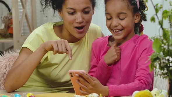 Mom and Daughter with Funny Bunny Ears Look at Phone and Enjoy Good News