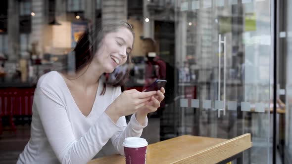 Young woman in a cafe enjoying a coffee and using a smartphone